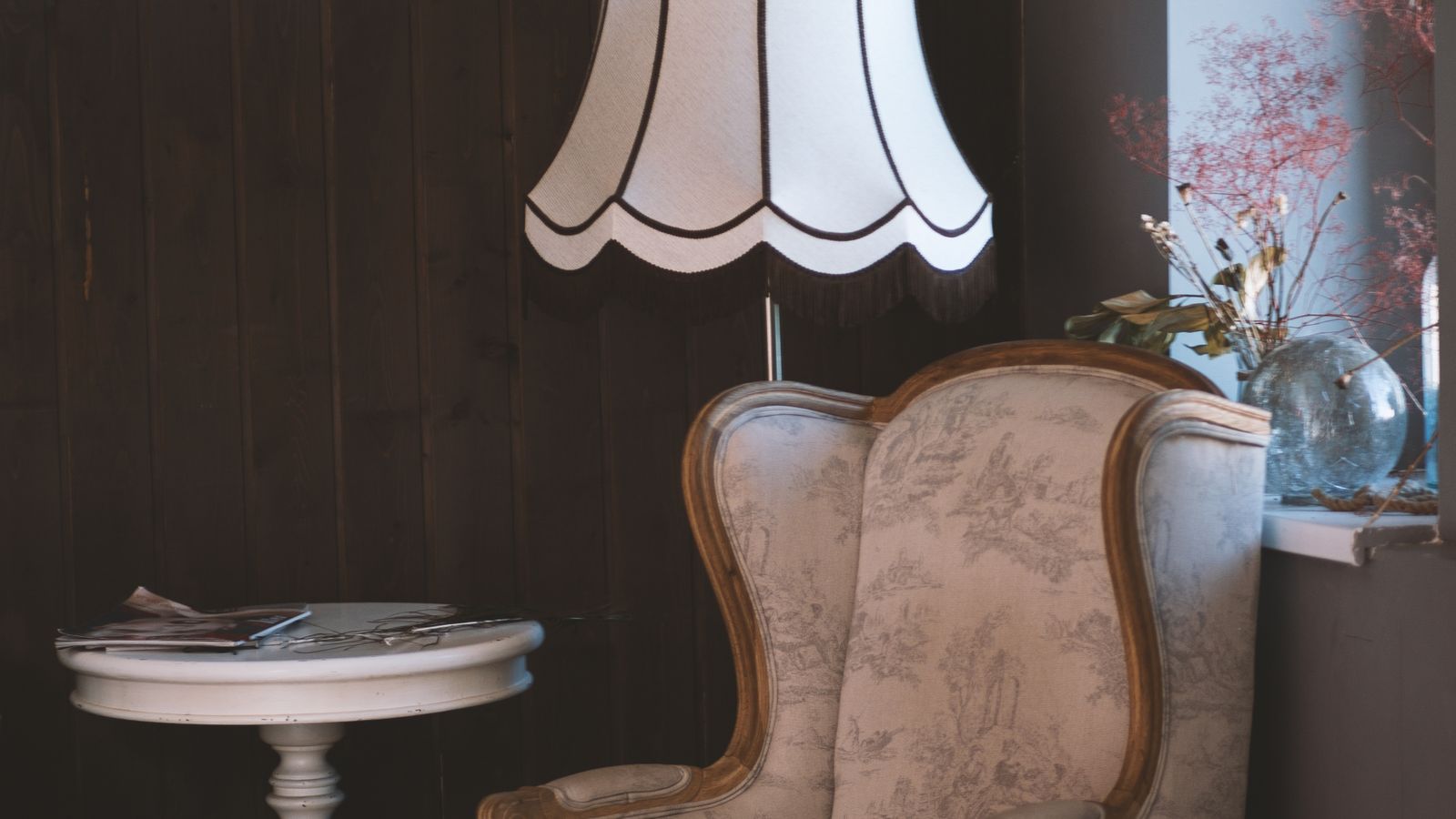 An upholstered armchair, a lamp and a side table in a dim room